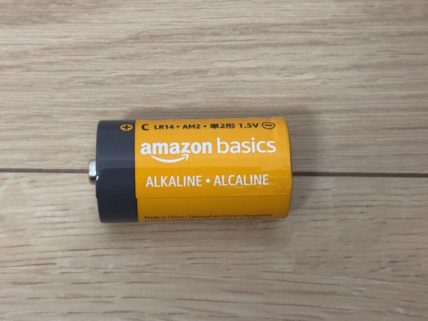 Amazonベーシックの単2形アルカリ乾電池1本。オレンジ色の本体にamazon basicsと書かれている
