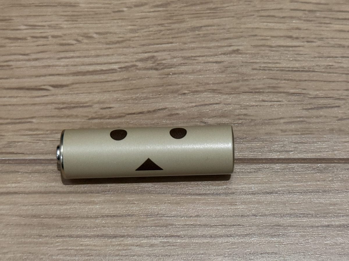 ダンボー柄の単3形充電池。金色の胴に、目と口を表した2つの丸と三角が描かれている