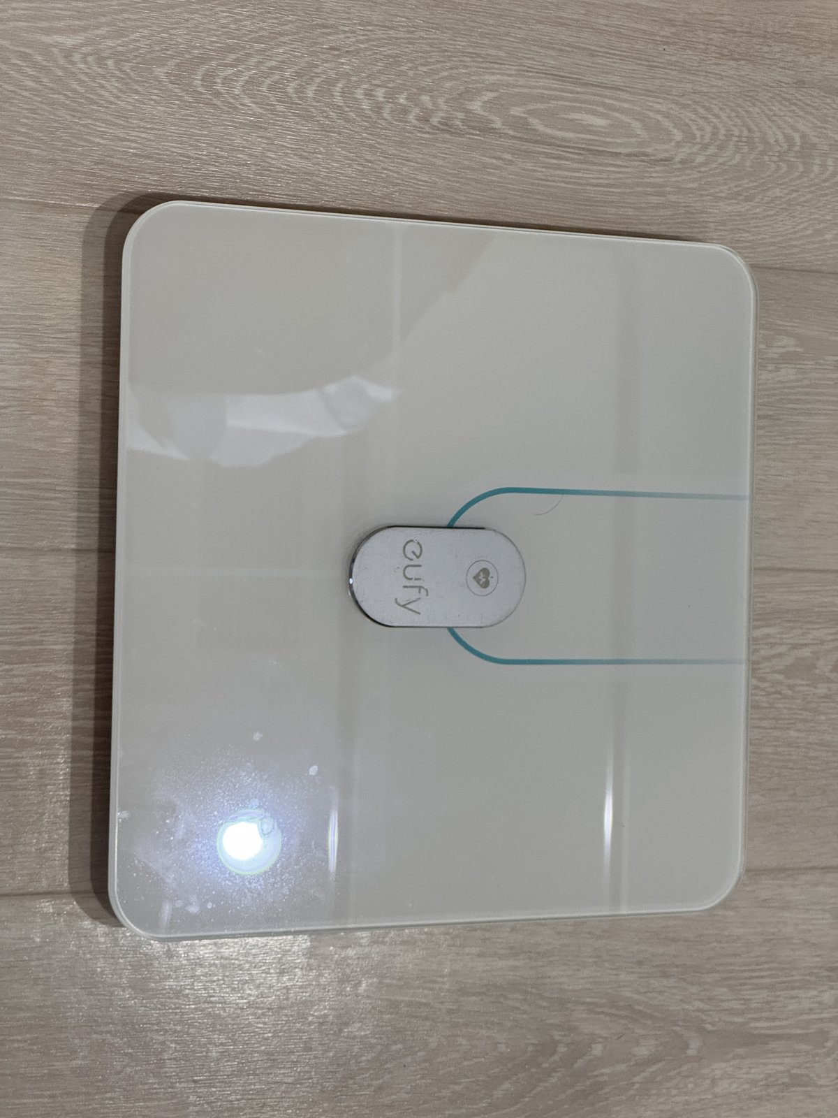eufyの白い正方形の体組成計。木の床に置かれ、中央にeufyのロゴがある