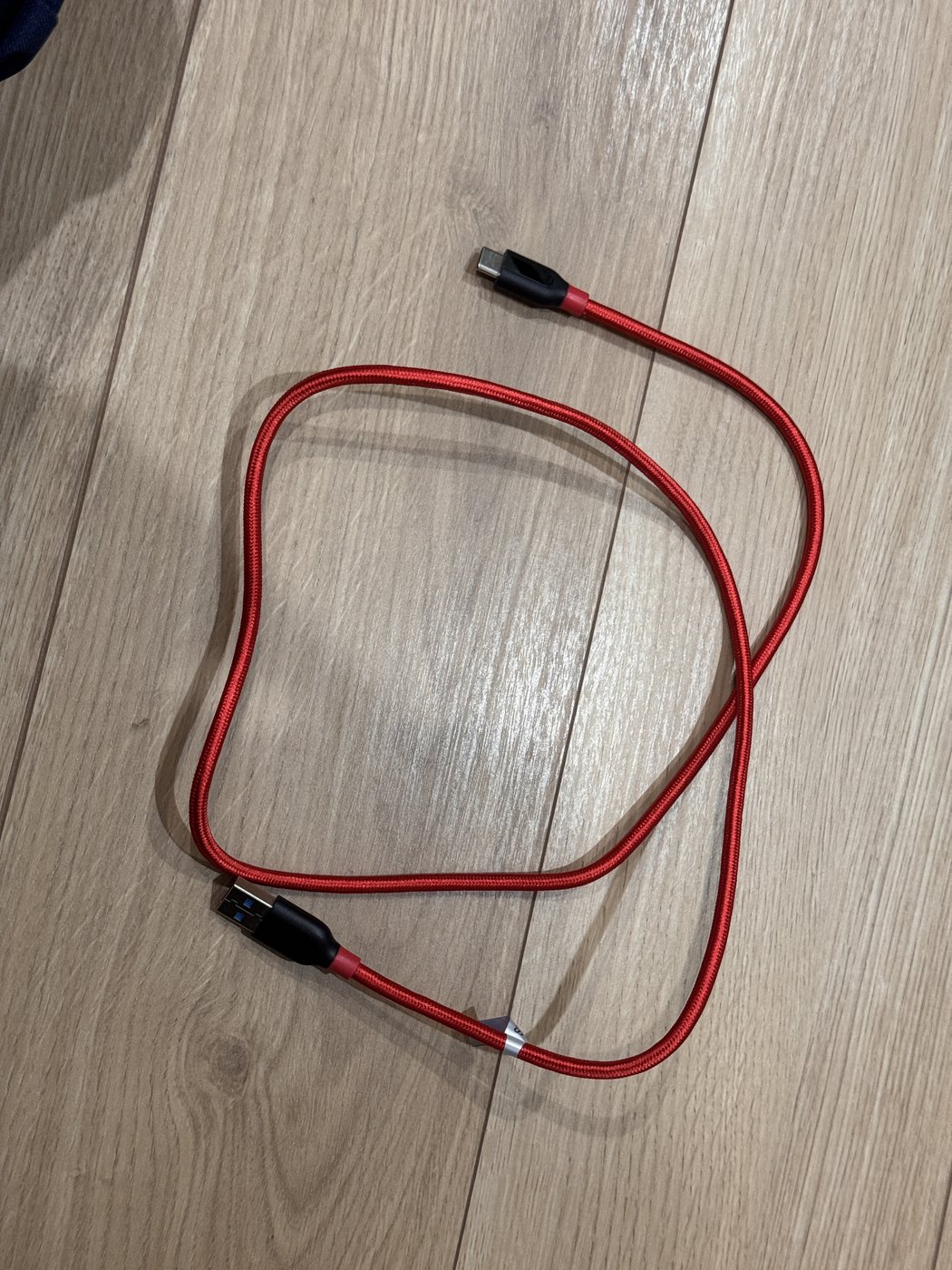 床に置いた赤い編み込みのAnker PowerLine+ケーブル。丸めても輪が広がって、癖がついたままになっている