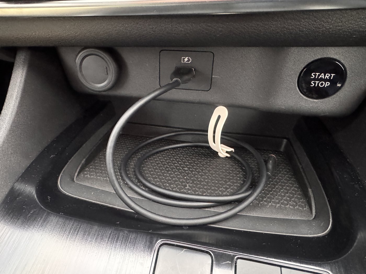 車のコンソールボックス手前にあるUSBの取り出し口に、黒いケーブルを挿したところ。右にエンジンのスタートストップボタンが見える
