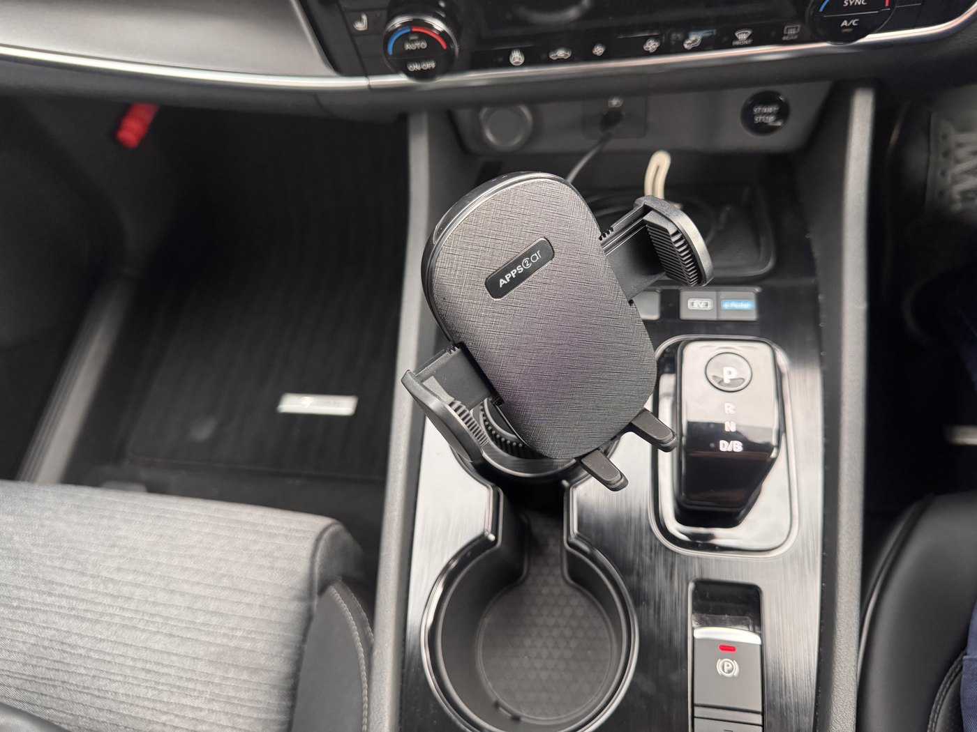 車のドリンクホルダーに挿したスマホホルダー。灰色の土台からアームが伸びて、スマホを挟むクリップが付いている