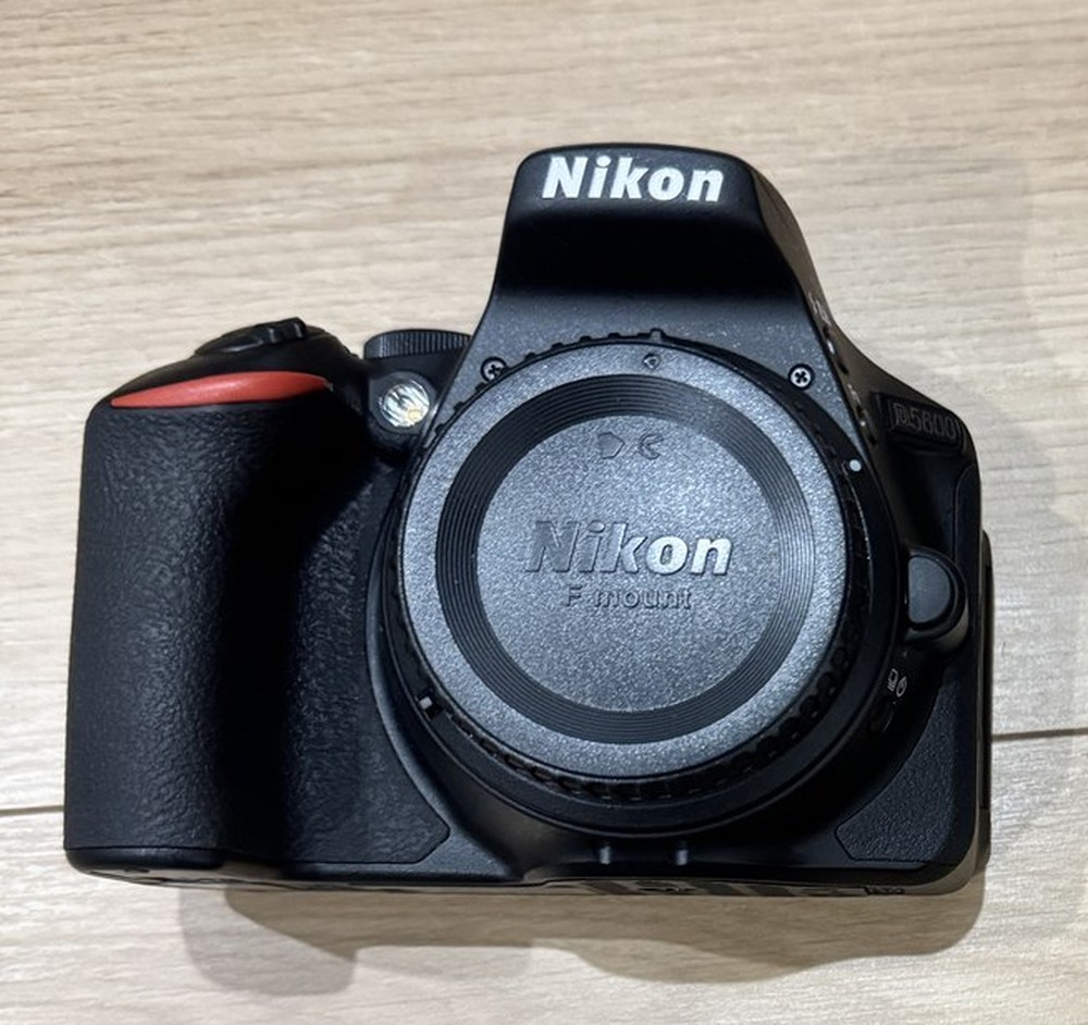 Nikon D5600の本体を正面から撮った写真。レンズを外してボディキャップが付いており、右側に D5600 の刻印、グリップの上に赤い差し色がある