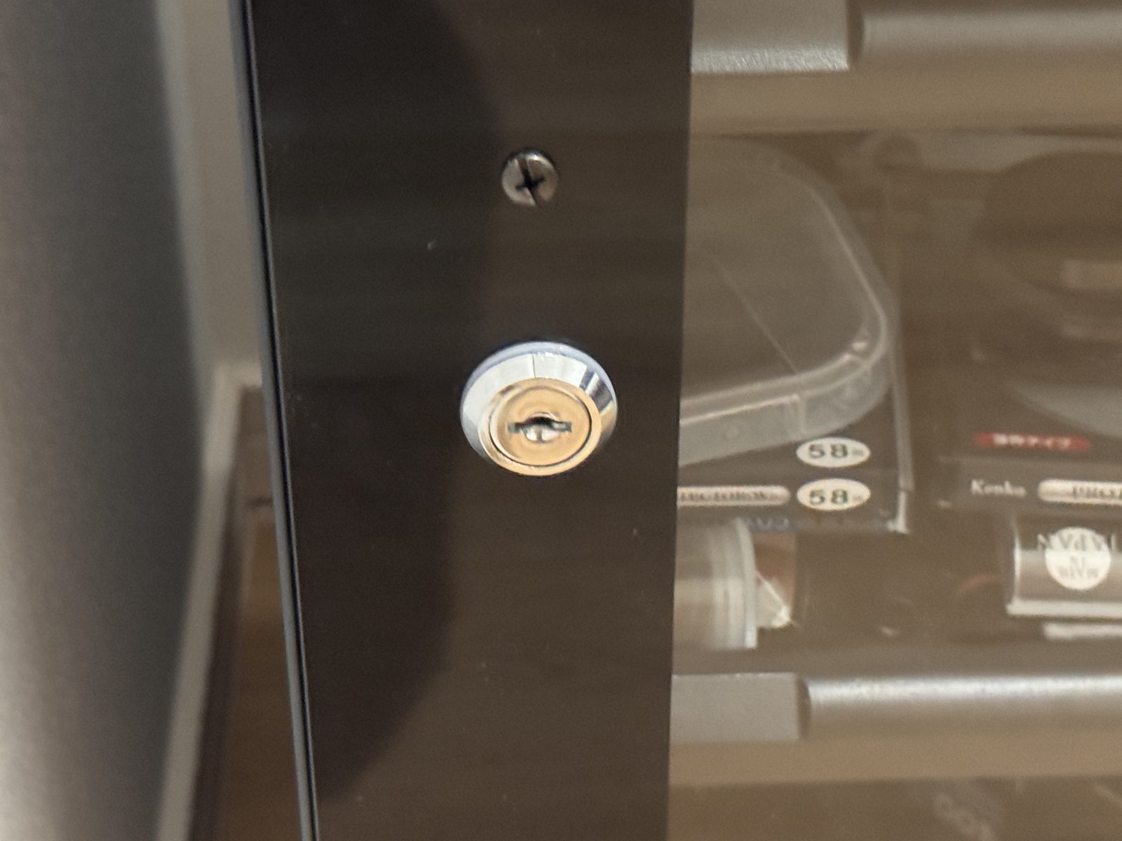 防湿庫の扉に付いた銀色の鍵穴のアップ。ガラス越しに保護フィルターのケースが見えている