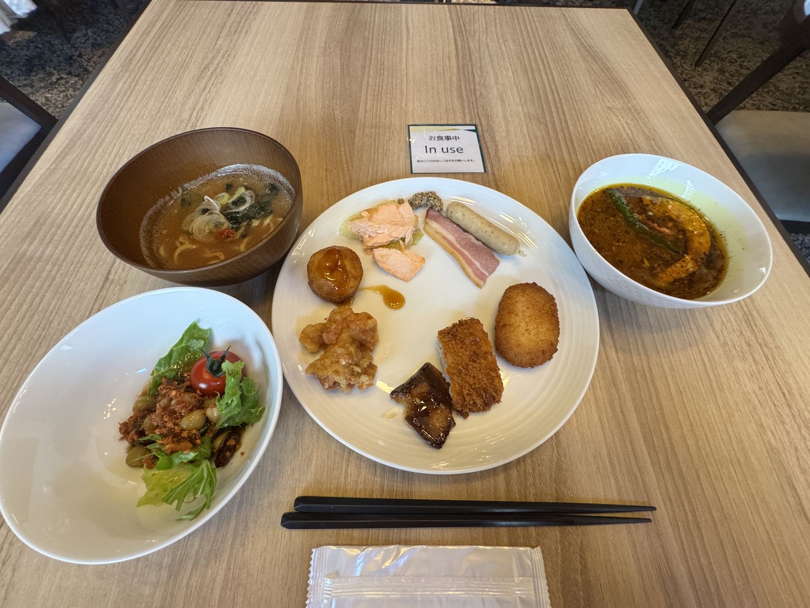 朝食のプレート。汁物、カレー、サラダ、揚げ物、ハム、卵