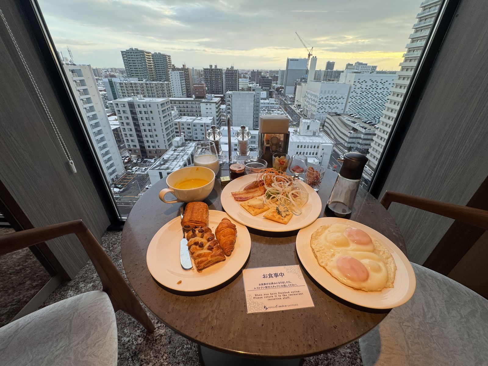 窓際のテーブルに置かれた朝食。パン、パンケーキ、スープ、サラダ、オレンジジュース