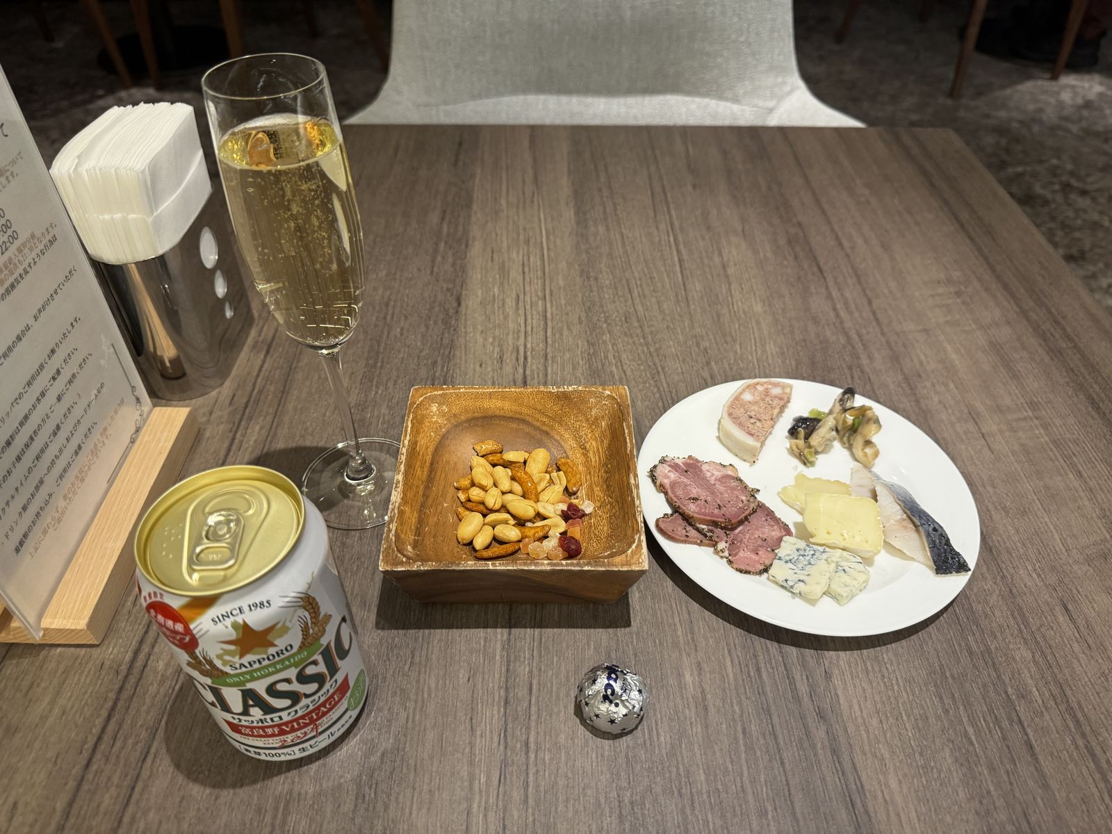 テーブルの上に、缶ビール、スパークリングワインのグラス、ナッツ、生ハムとチーズの皿