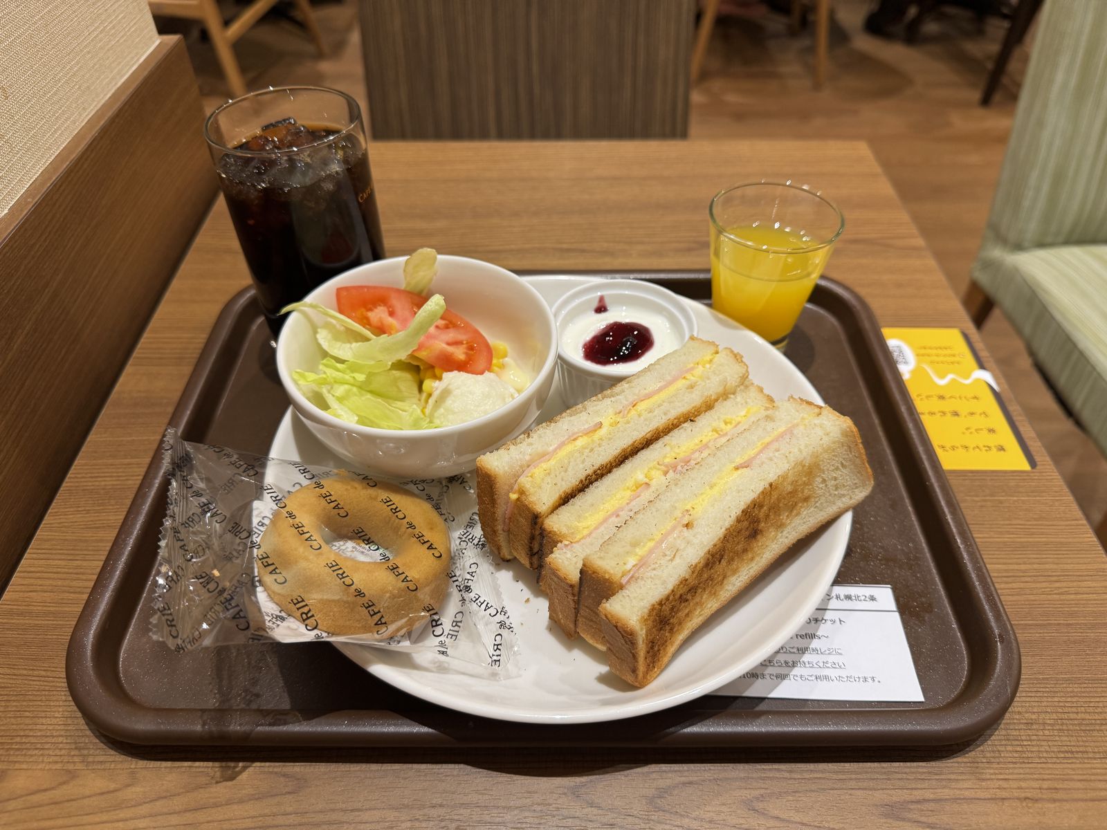 朝食のトレー。サンドイッチ、ベーグル、サラダ、ジャム、オレンジジュース、アイスコーヒー