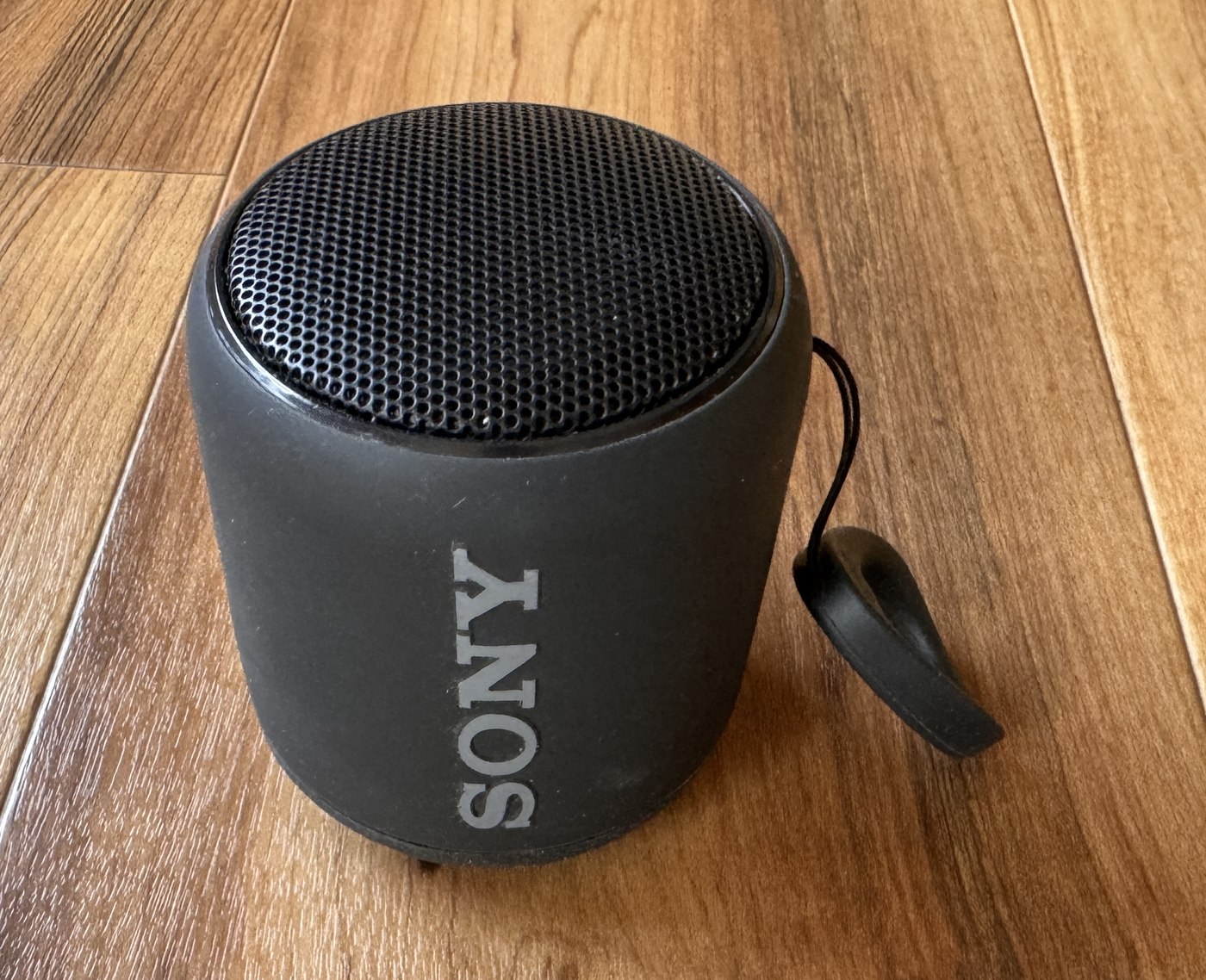 木の床に置いたソニーのSRS-XB10。黒い円筒形で、上の面が網目になっており、横にSONYのロゴと持ち運び用のひもが付いている