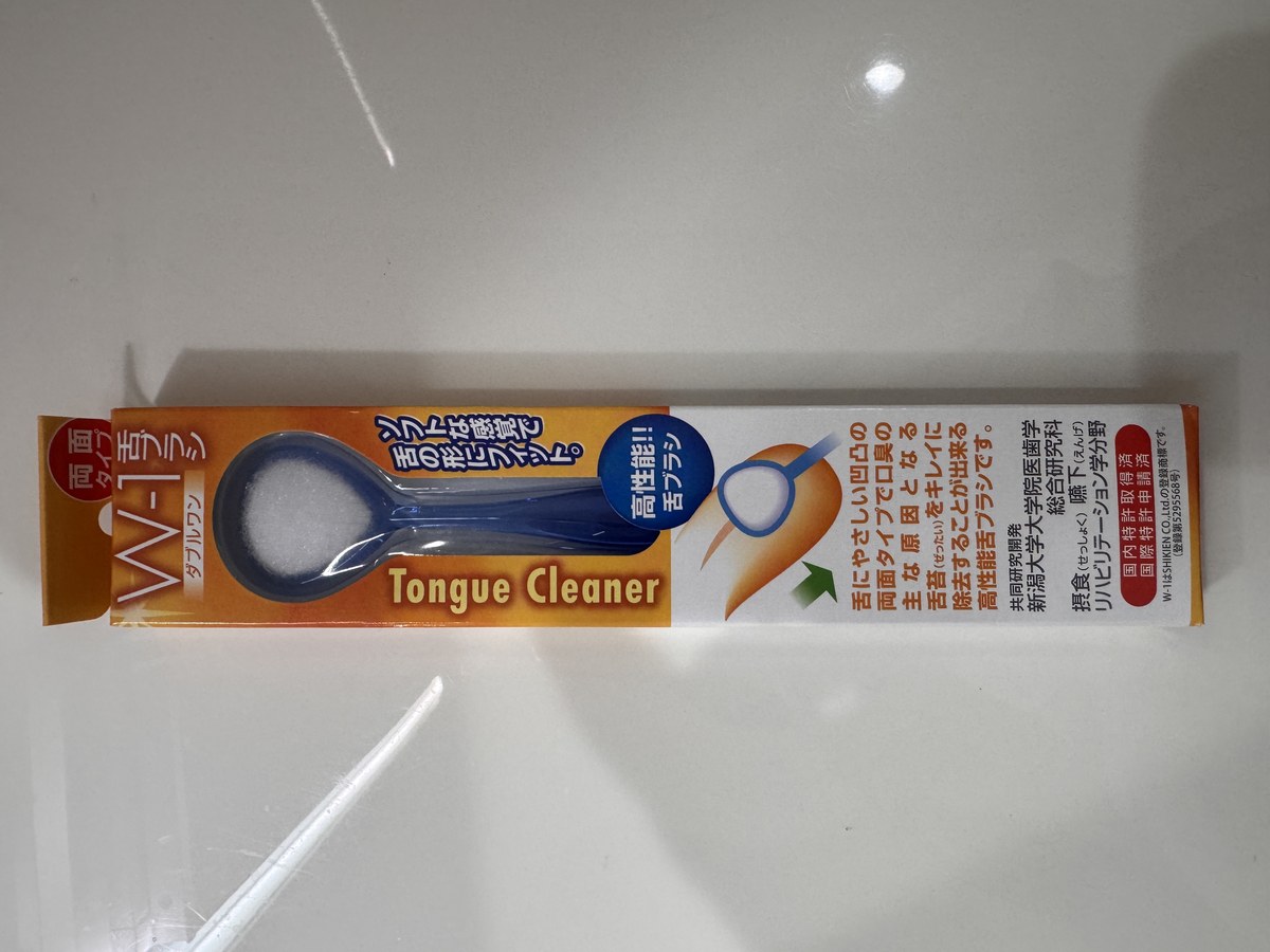 オレンジ色の箱に入った青い舌クリーナー。Tongue Cleaner W-1 と書かれている