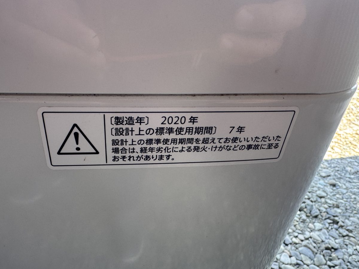 洗濯機の側面に貼られた注意ラベル。製造年2020年、設計上の標準使用期間7年と印刷されている