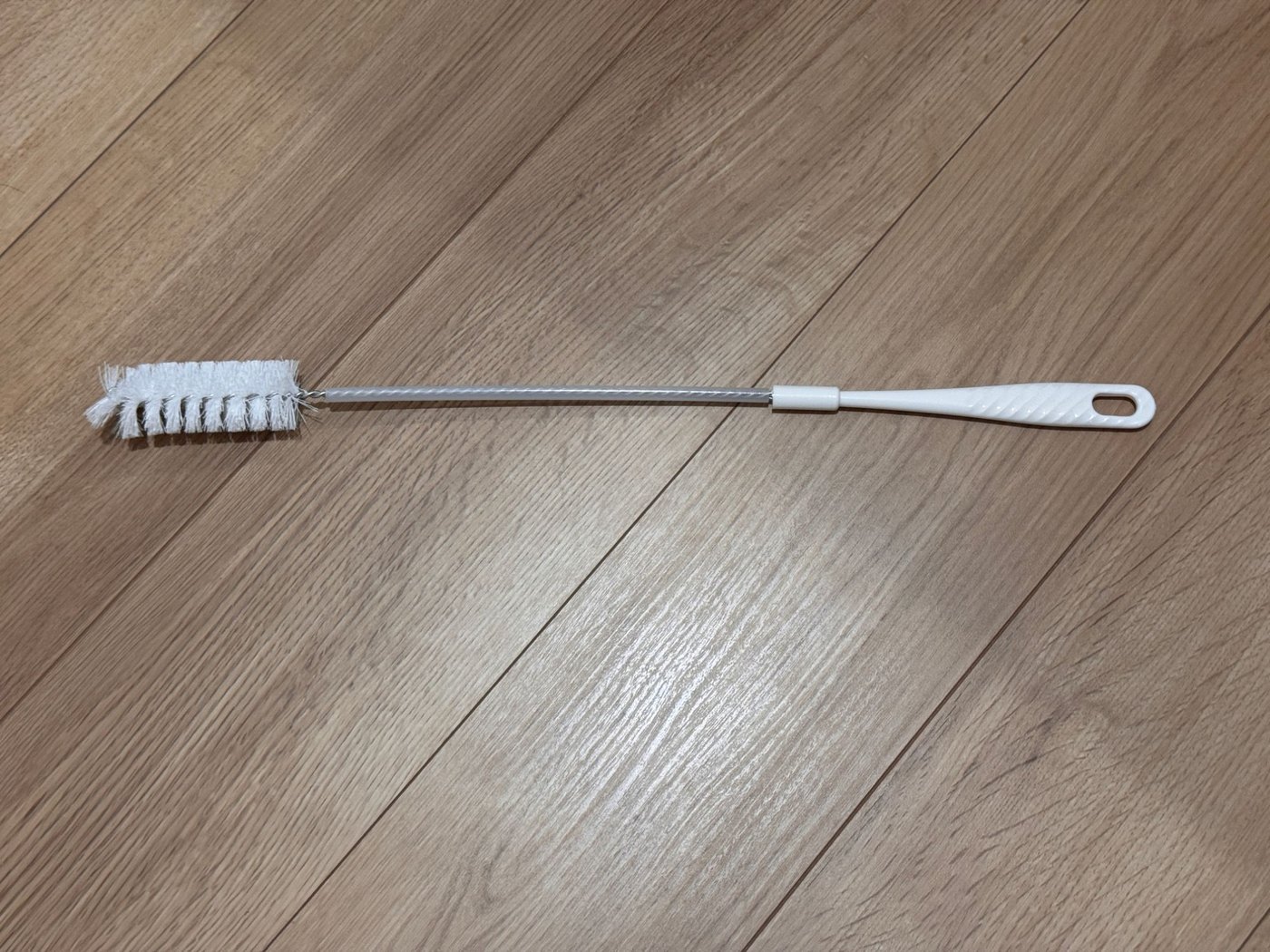 木の床に置いたパナソニック純正のおそうじブラシ。白い持ち手から細長い柄が伸び、先に円筒形の白いブラシが付いている